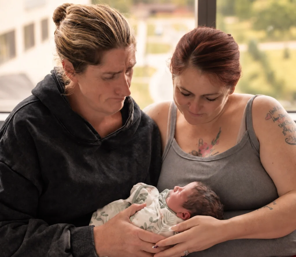 Intended Parent and Gestational Carrier holding a newborn together